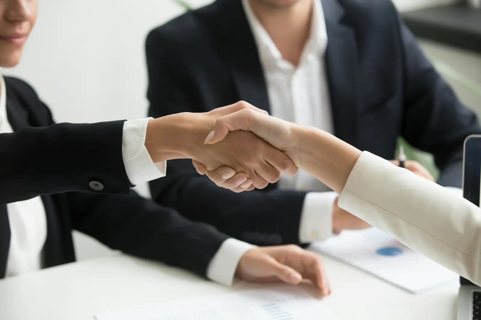 Two business people shaking hands beside an open laptop