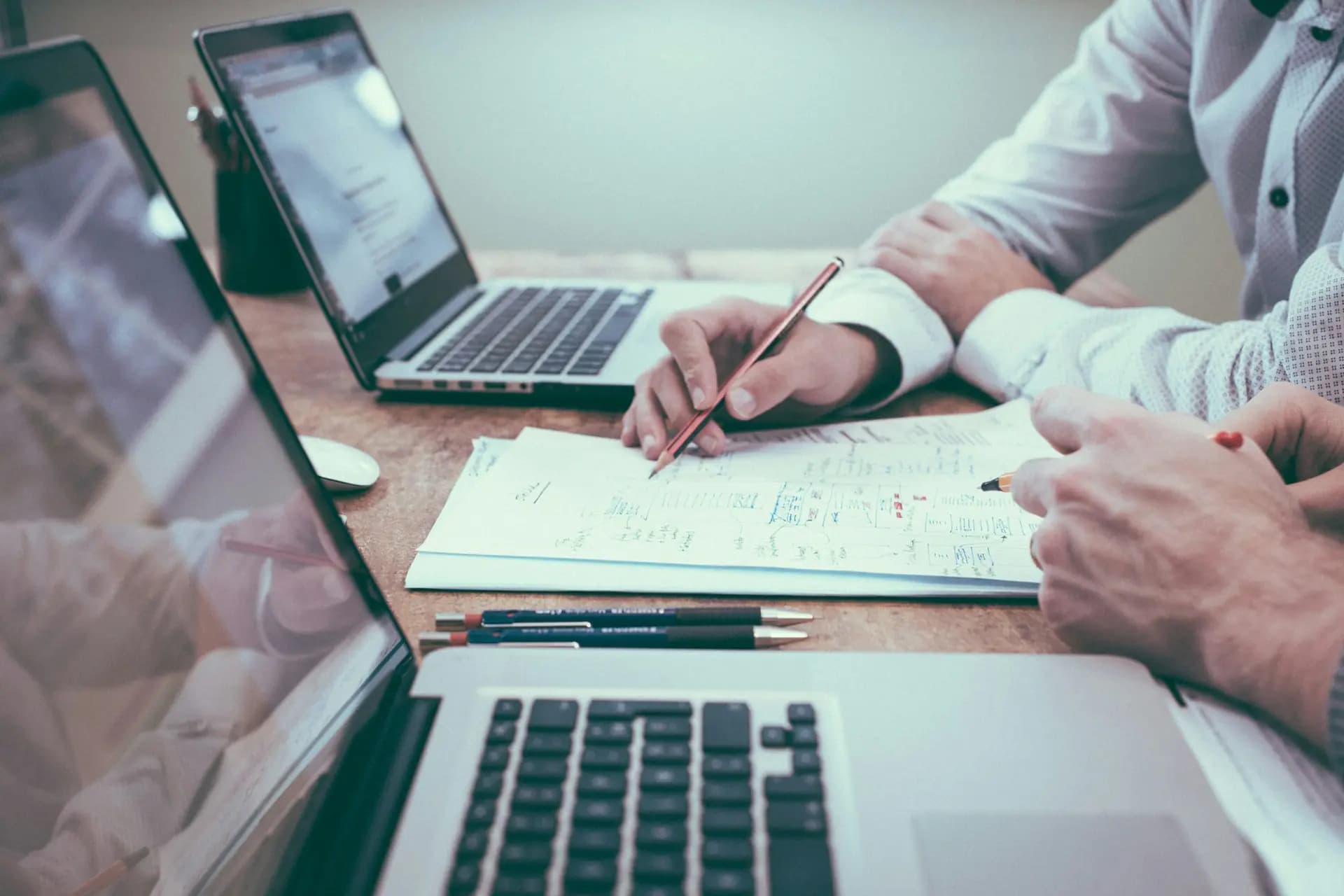 Two people reviewing paperwork beside open laptops