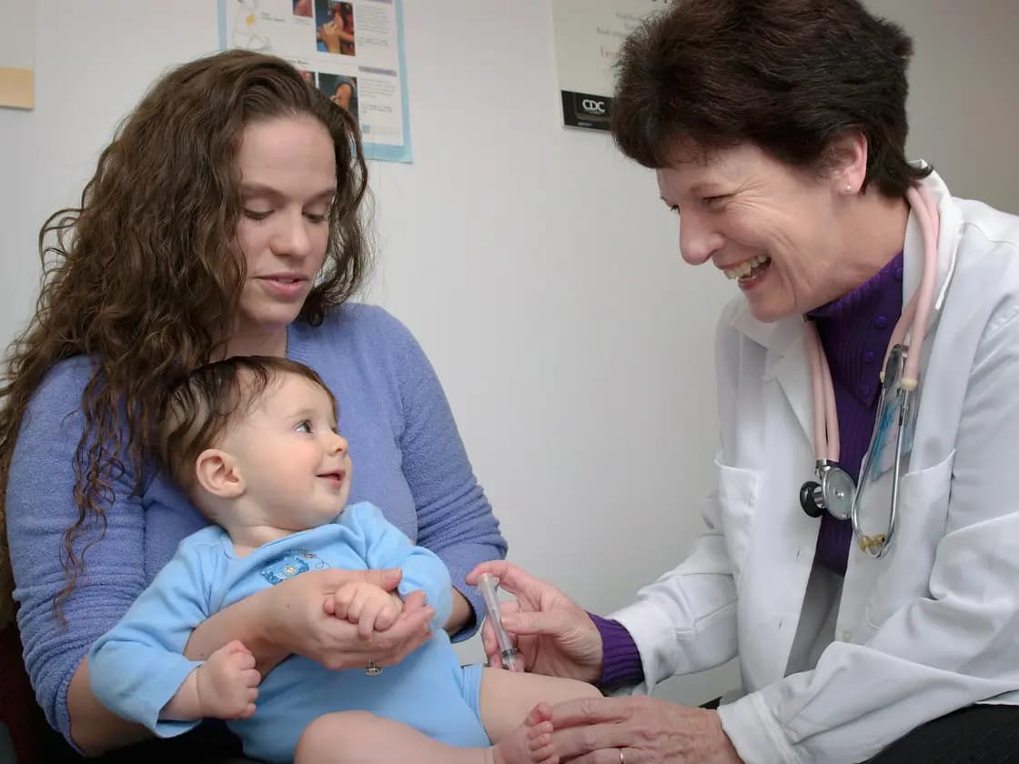 A smiling doctor checking a baby held on the lap of their mother