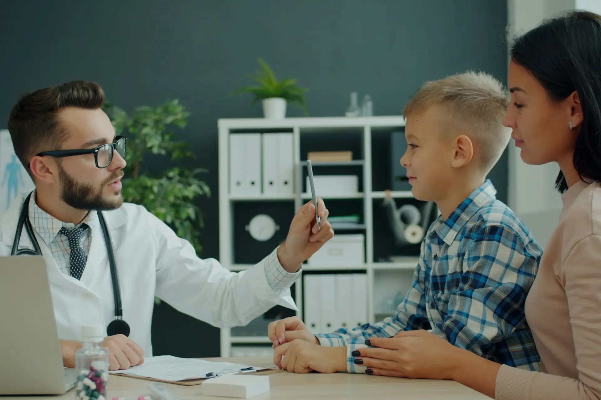 A doctor talking with a young boy and his mother across a desk in a clinic